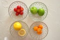 Green jujube, kumquats, lemons, small tomatoes in glass bowls, top view, marble background