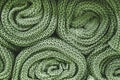 Green knitted blankets rolled into rolls. Knitted texture, factory textiles