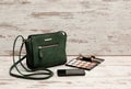 Green ladies handbag, phone, eyeshadow palette and a lipstick on a wooden background. fashion concept