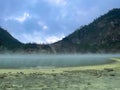 Green lake mirrored with fog above and green cliffs as a background