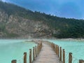 Green lake mirrored with fog over it and wooden bridge leading to green cliffs