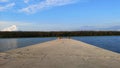 View of the beautiful breakwater that goes into the distance. Green landscape intersected with blue sky.