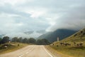 Green landscape with road. Cloudy sky, cows grazing, mountains n the background Royalty Free Stock Photo