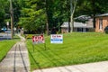 A green lawn in front of a house with two for sale signs on a sunny day