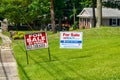 A green lawn in front of a house with two for sale signs on a sunny day