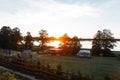 Green lawn with a tent with a gazebo with a trampoline with a wooden fence against the backdrop of an orange sunset and a lake. Royalty Free Stock Photo