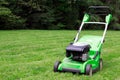 A green lawnmower in the garden. A lawn mower on the green grass. Gardening