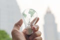 Hands holding Tungsten light bulb with green earth map