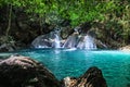 Green leaves on top and rocks in front frame a beautiful short waterfall with smooth rocks in the dense forest of Erawan Royalty Free Stock Photo