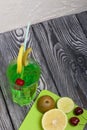 Green lemonade in a glass. Cherry floats in it. Garnished with a slice of lemon and kiwi. With a straw for a cocktail. Nearby on a Royalty Free Stock Photo