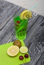 Green lemonade in a glass. Cherry floats in it. Garnished with a slice of lemon and kiwi. With a straw for a cocktail. Nearby on a Royalty Free Stock Photo