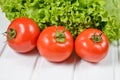 Green lettuce leaves, ripe red tomatoes on a white wooden table. Royalty Free Stock Photo