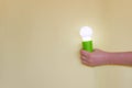 Green Light bulb on yellow background. Hand holds lamp. Free copy space. Concept of new idea, green energy Royalty Free Stock Photo
