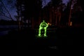 Green Light painting of human sitting on bench in dark night landscape with long exposure and glow of yellow fire light