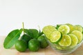 Green limes with leaves and sliced lime in glass bowl on wood, white background. Royalty Free Stock Photo