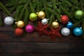 Green living spruce branches on a dark wooden background. New Year background with red stars and colorful balls. Top view