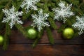 Green living spruce branches on a dark wooden background. New Year background with green balls and white snowflakes. Top view