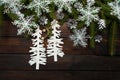 Green living spruce branches on a dark wooden background. New Year background with cones and white snowflakes and cardboard Christ