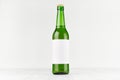 Green longneck beer bottle 500ml with blank white label on white wooden board, mock up.