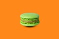 Green macaron isolated on orange background. with a shadow