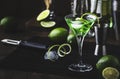 Green martini alcoholic cocktail in glass with dry gin, vermouth, liquor, lime zest and ice, steel bar tools, dark background Royalty Free Stock Photo