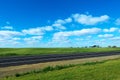 Green meadow with asphalt road and blue sky Royalty Free Stock Photo