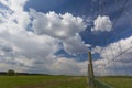 Green meadow with country road, clouds and fence on foreground