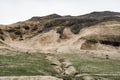 A green meadow with a furrow for the gathering of mountain water, with green grass. Against the backdrop of a hill with