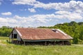 Green meadow with old pole barn, open side filled with hay bales, rusted tin roof, blue sky copy space