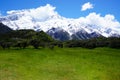 Green meadow with snow capped mountains under blue sky Royalty Free Stock Photo