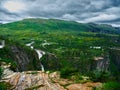 Green meadow surrounded by green mountain slopes and a rocky mountain with a waterfall, with clouds