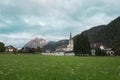 Green Meadows, Wooden Houses and Church in the Village of San Vigilio di Marebbe and Italian Alps Mountains in the Background on a Royalty Free Stock Photo