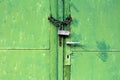 Green metal doors with cracked paint and dilapidated door handle locked with rusted chain and old padlock