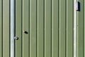 Green metal fence and doors made of corrugated steel sheet with vertical rails and a surveillance camera Royalty Free Stock Photo