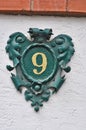 A green, metal heraldry decorated house number plaque, fixed on a wall, showing the number nine Royalty Free Stock Photo