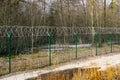 A green metal mesh fence with coiled barbed wire around the restricted area of a military facility