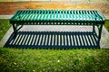 Green metal park bench on concrete slab by brick sidewalk with dramatic shadow Royalty Free Stock Photo