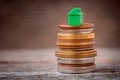 Green miniature home on the stack of various coins