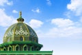 A green mosque dome with bright clouds