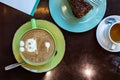 Coffee latte art on drown wooden table top view. Latte hot coffee in a green cup with latte art served with piece of orange- Royalty Free Stock Photo