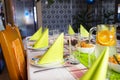 Green napkins arranged on plates in the shape of a triangle, lemonade made of water and orange slices in a large jug, salads visib