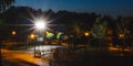 Green night empty playground in park with bright spotlight on blue background. Evening city urban landscape. Nobody in Royalty Free Stock Photo