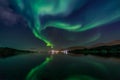 Green Northern lights reflecting in the lake with mountains and