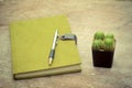 Green notebook, pen and cactus pot on wooden desk - vintage style Royalty Free Stock Photo