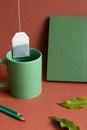 Green object. Cup of tea, notebook, colored pencil on red background