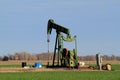 Green oil well pump in a farm field with green wheat and blue sky in Kansas out in the country. Royalty Free Stock Photo