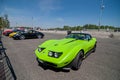 A green old Chevrolet Corvette C3 Stingray sports car stands in a gray concrete parking lot.