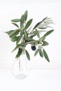 Green olive branches in glass vase on a white brick wall background. Wall mockup. Minimal home decor. Simple modern interior