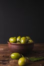 Green olives in a ceramic bowl on a wooden background.