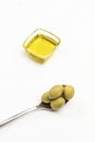 Green olives in metal spoon. Olive oil in glass jar